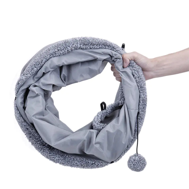 Gray fleece-lined infinity scarf with pom-pom held by a hand on a white background
