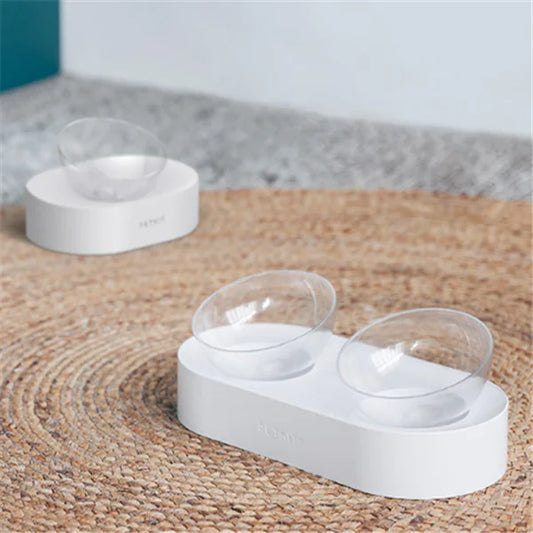 Adjustable raised cat feeder with two clear tilted bowls on white stand